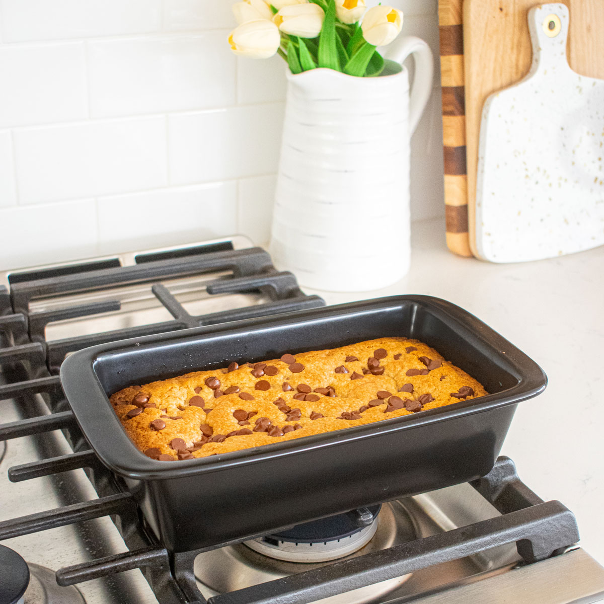 xtrema loaf pan with banana chocolate chip cookie bars baked inside cooling on top of an oven.