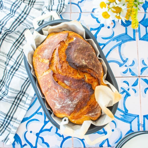 golden brown sourdough discard bread with bone broth in a bread oval on a blue tile table with fresh flowers.