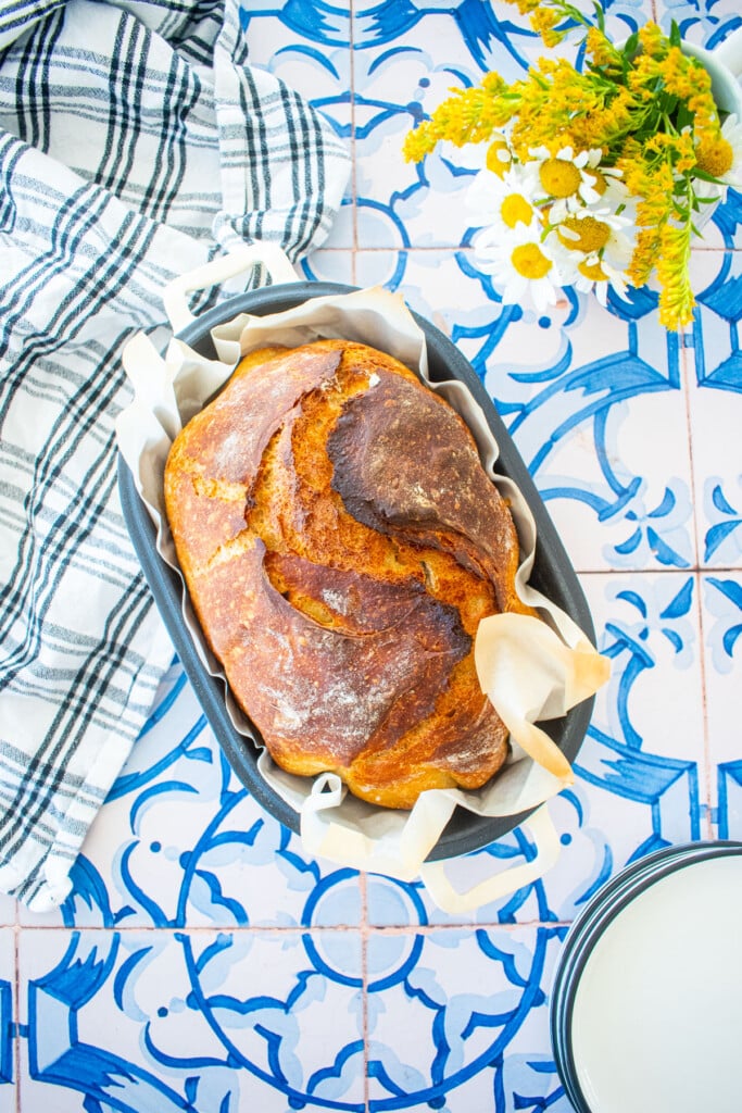 golden brown sourdough discard bread with bone broth in a bread oval on a blue tile table with fresh flowers.