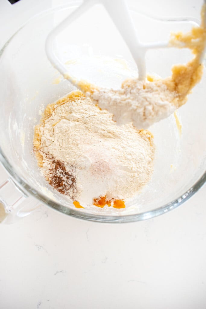 ingredients for pumpkin cake in a glass mixing bowl on a marble counter.