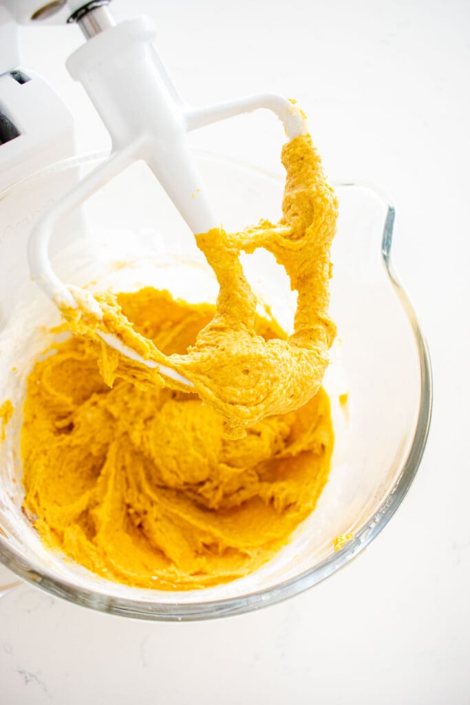 pumpkin cake batter in a glass mixing bowl on a marble counter.