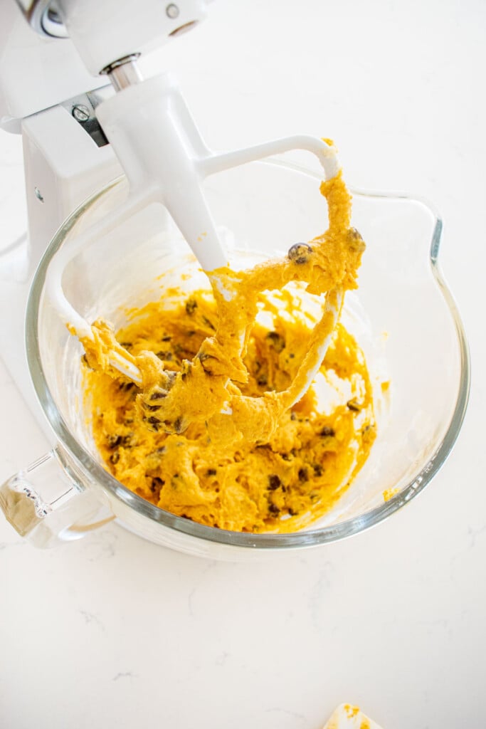 glass mixing bowl with pumpkin chocolate chip cake batter on a marble counter.