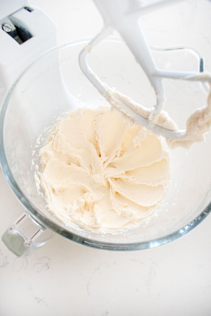white decorating frosting in a glass mixing bowl on a marble counter.