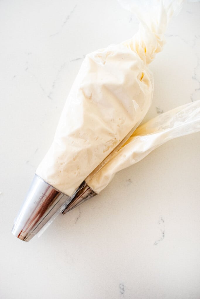 two piping bags with white decorating frosting on a marble counter.