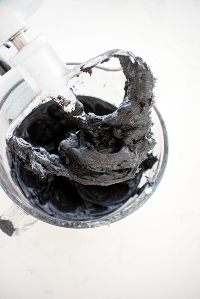 black frosting in a glass mixing bowl on a marble counter.