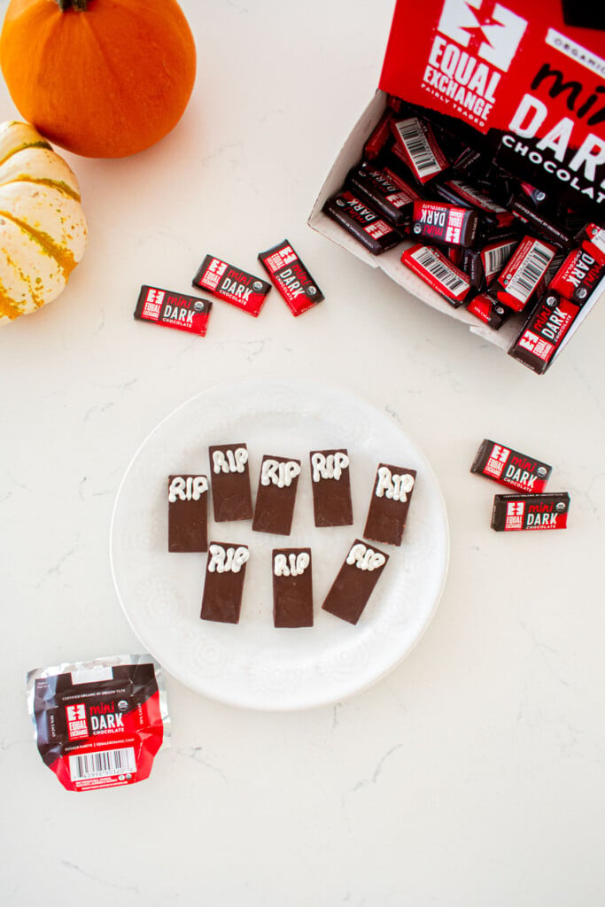 small chocolate bars with RIP written in white frosting on a plate on a marble counter with tiny pumpkins.