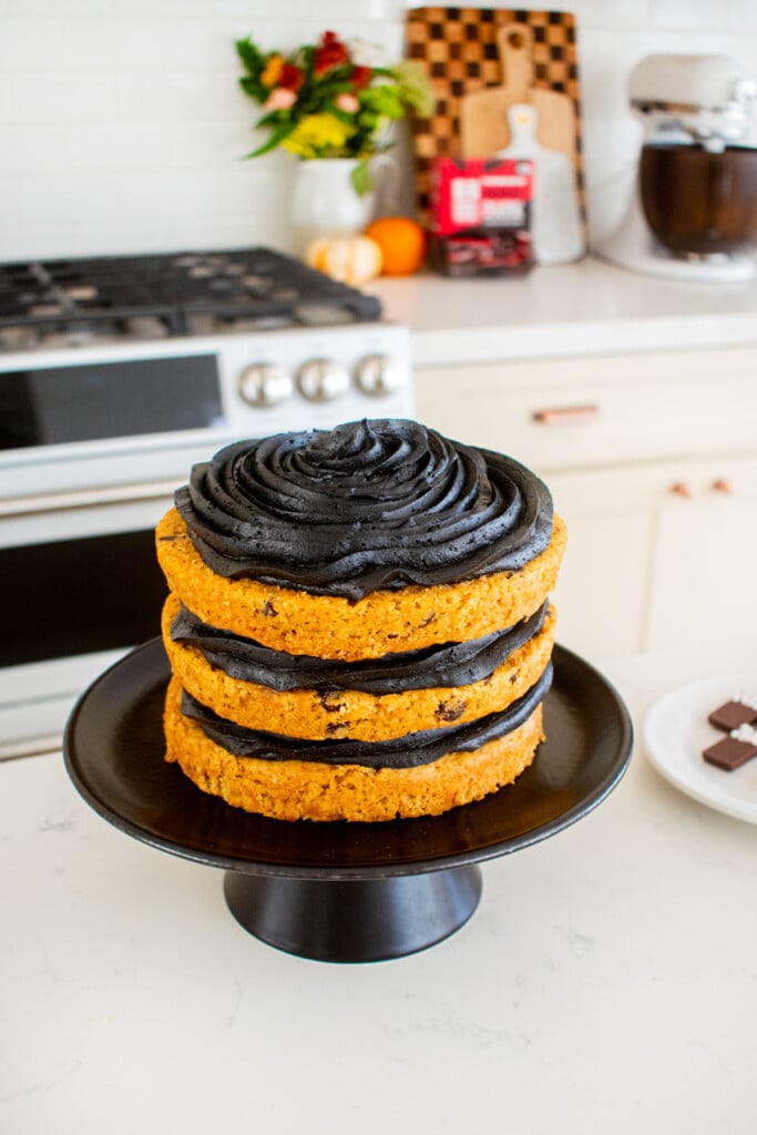 pumpkin chocolate chip naked cake with black frosting on a cake stand on kitchen counter.