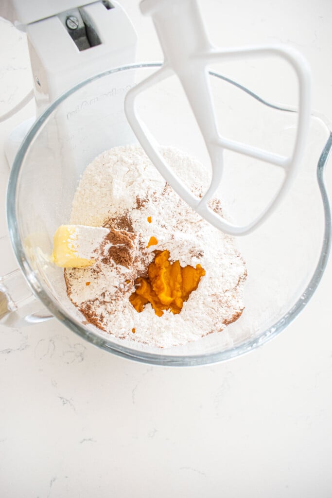 ingredients for pumpkin spice buttercream frosting in a glass mixing bowl on a marble counter.