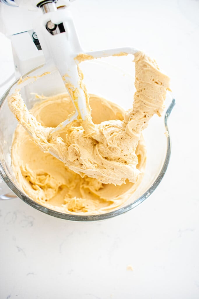 smooth and creamy pumpkin spice buttercream frosting in a glass mixing bowl on a marble counter.