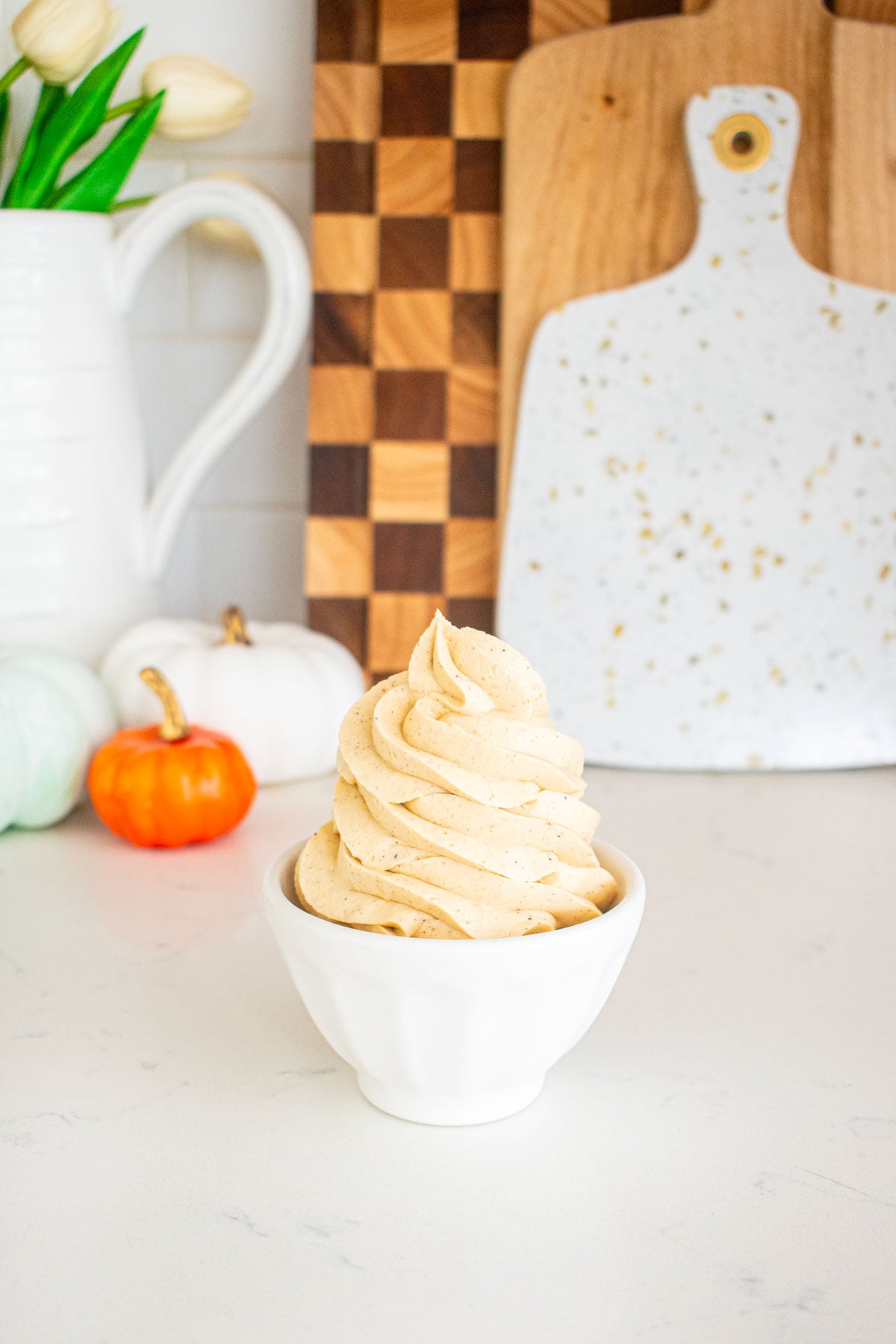 small dish with a piped swirl of pumpkin spice buttercream frosting on a marble counter.