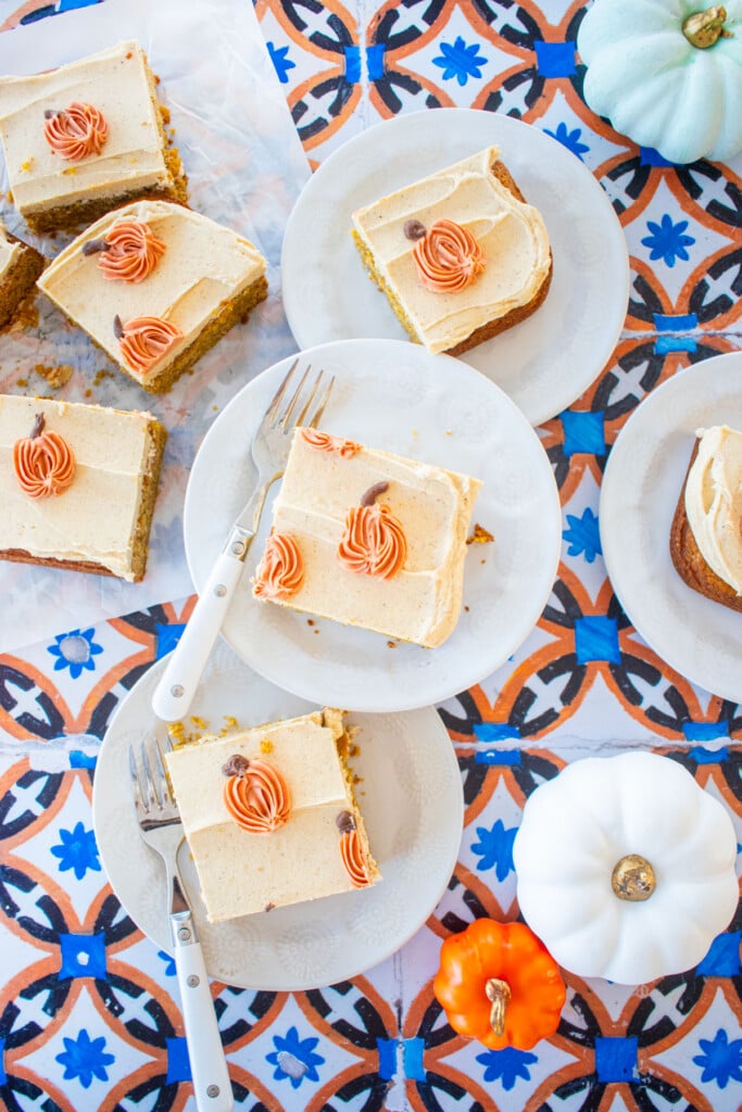 dessert plates with square slices of pumpkin spice cake with pumpkin spice buttercream and piped pumpkins on top on a tile table.