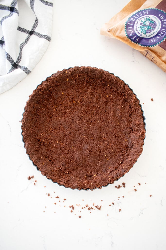 chocolate graham cracker crust formed into a tart pan on a marble counter.