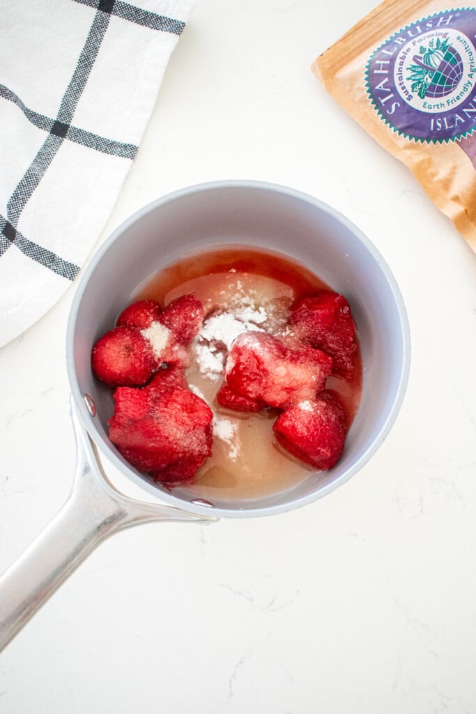 ingredients for strawberry compote in a small pot on a marble counter.