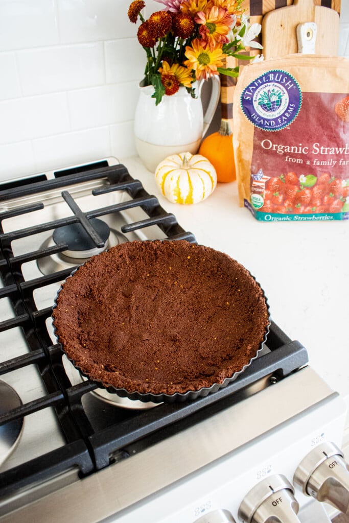 baked chocolate graham cracker crust cooling on top of an oven.