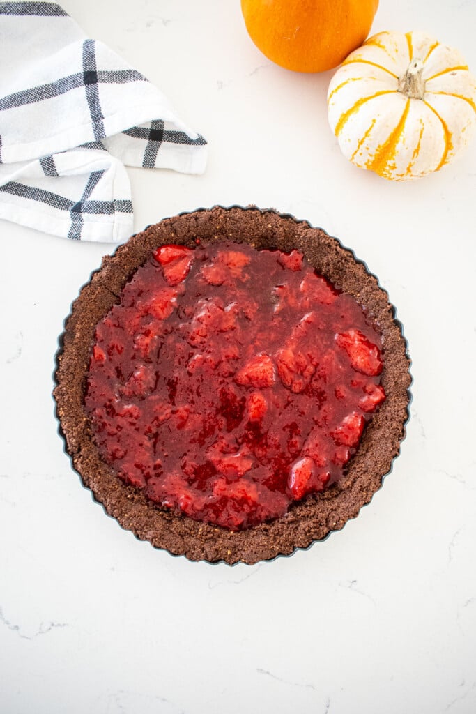 chocolate graham cracker crust with strawberry compote inside on a marble counter with tiny pumpkins.