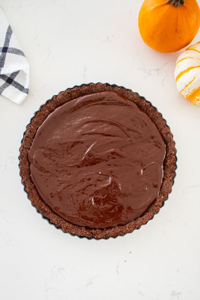 chocolate graham cracker crust with chocolate ganache inside on a marble counter with small pumpkins.