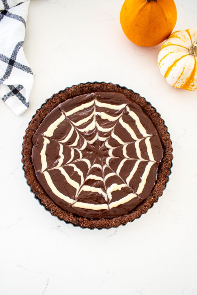spider web chocolate strawberry tart on a marble counter with tiny pupmkins.