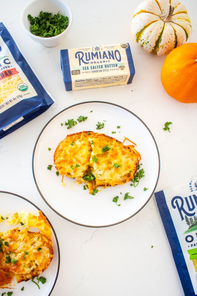 plate of cheesy pumpkin garlic bread with fresh parsley on a marble counter with tiny pumpkins and bags of shredded cheese.