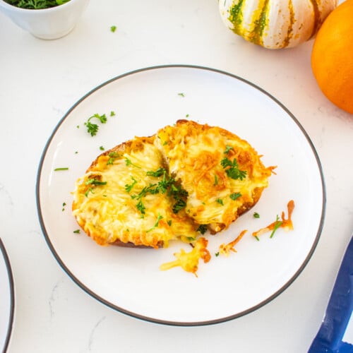 plate of cheesy pumpkin garlic bread with fresh parsley on a marble counter with tiny pumpkins and bags of shredded cheese.
