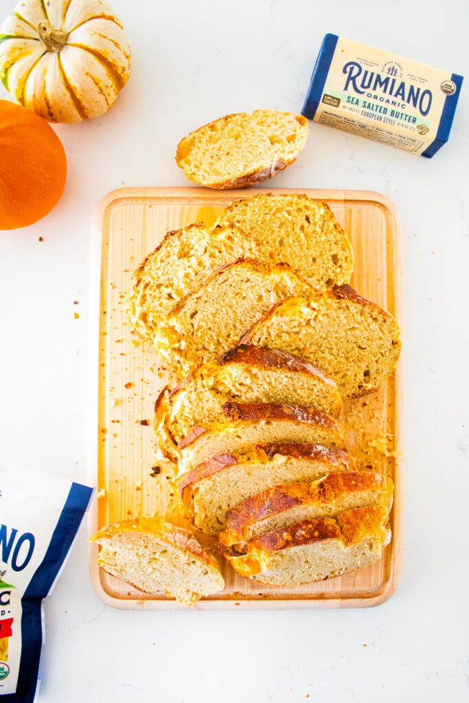 wood cutting board with bread sliced on a marble counter with tiny pumpkins.