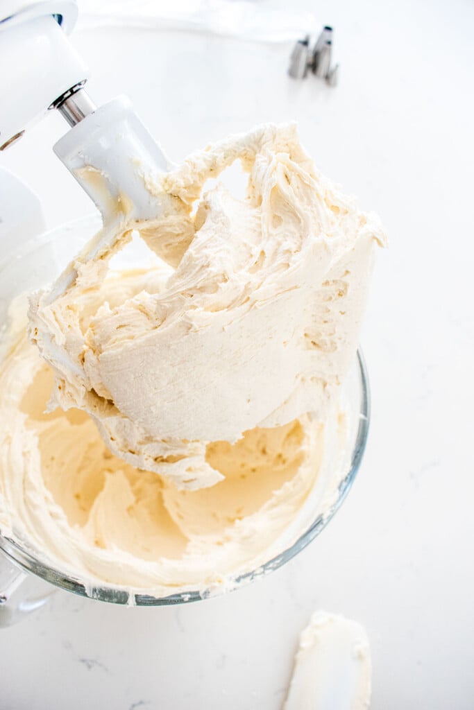 vanilla decorating frosting in a glass mixing bowl on a marble counter.