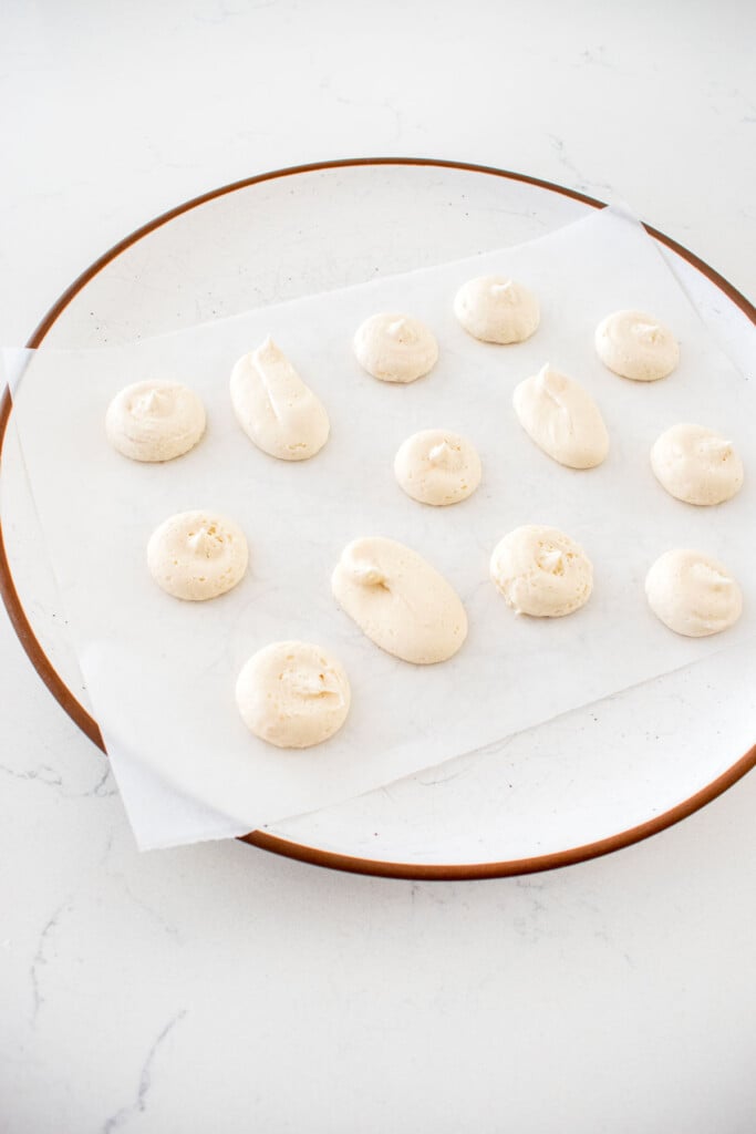 plate with parchment paper and piped dollops of vanilla buttercream frosting on a marble counter.