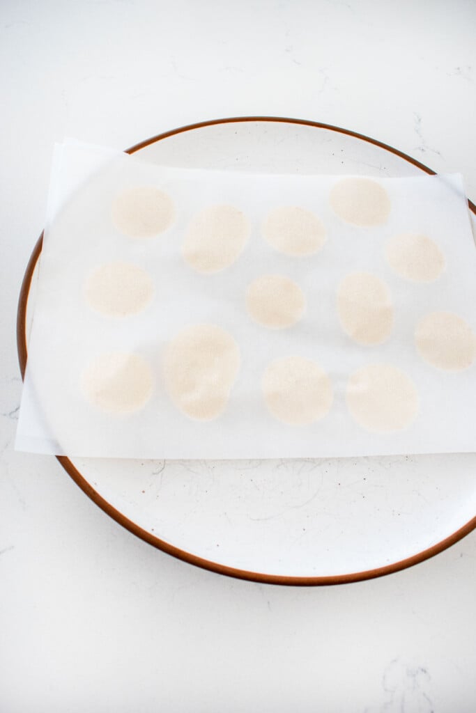 plate with parchment paper and piped dollops of vanilla buttercream frosting with a piece of parchment paper pressed over the top.