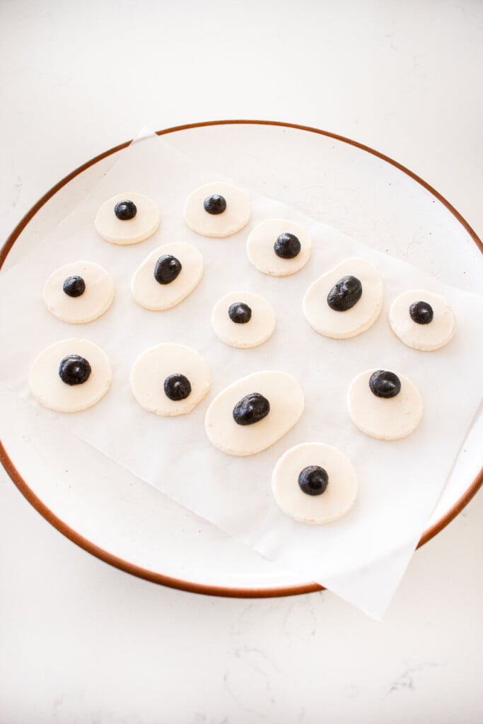 monster eyes piped onto a piece of parchment paper on a plate on a marble counter.