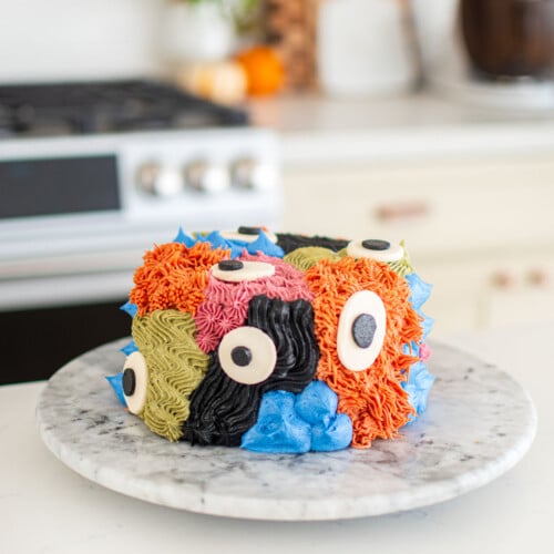 monster cake with different colored textures and big eyes on a marble turn table on a kitchen counter.