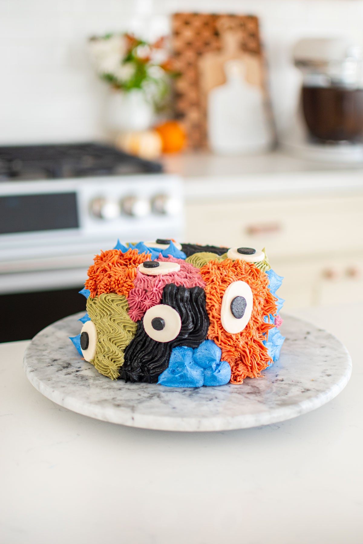 monster cake with different colored textures and big eyes on a marble turn table on a kitchen counter.
