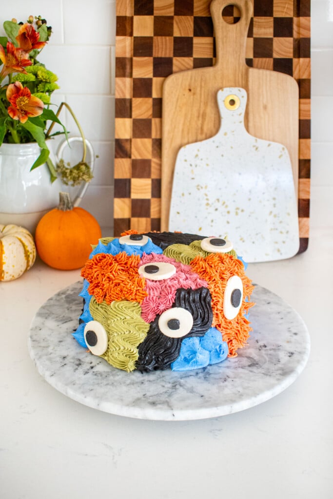 monster cake with different colored textures and big eyes on a marble turn table on a kitchen counter.